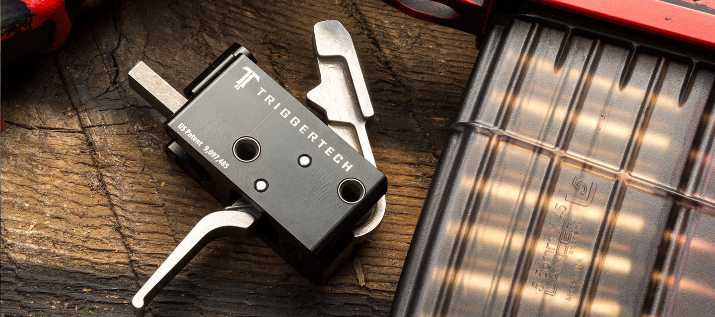 A TriggerTech trigger assembly and a loaded magazine resting on weathered wood